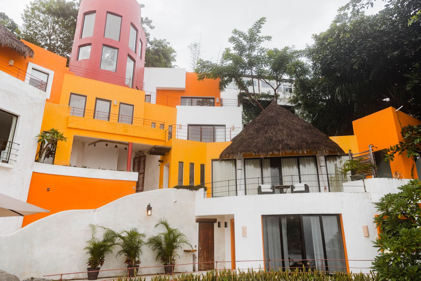 Orange and white villa facades with a pink tower and a thatched palapa roof at Villa Mandarinas