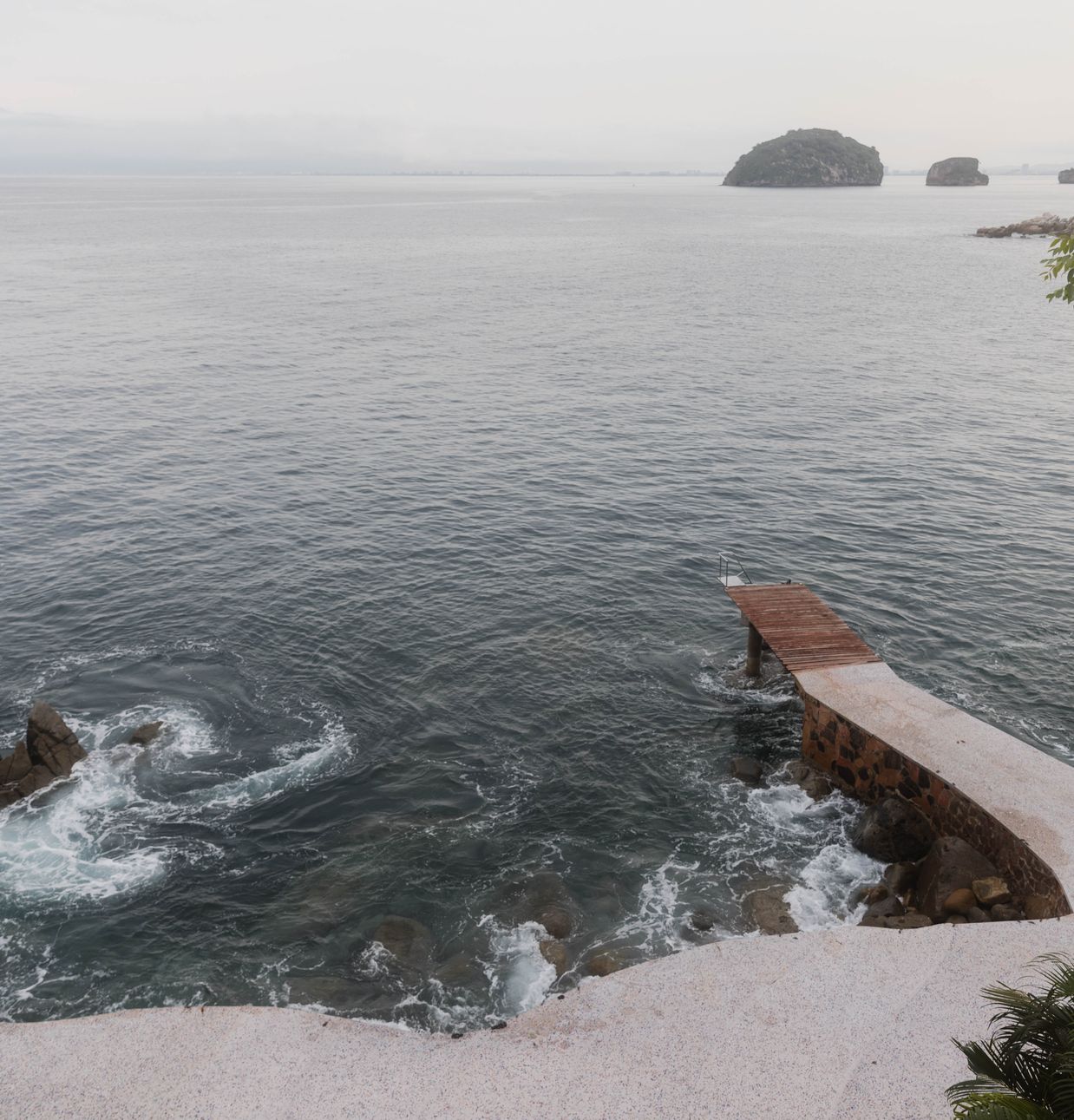 Rocky coastline with a private pier below Villa Mandarinas and the Los Arcos islets in the bay