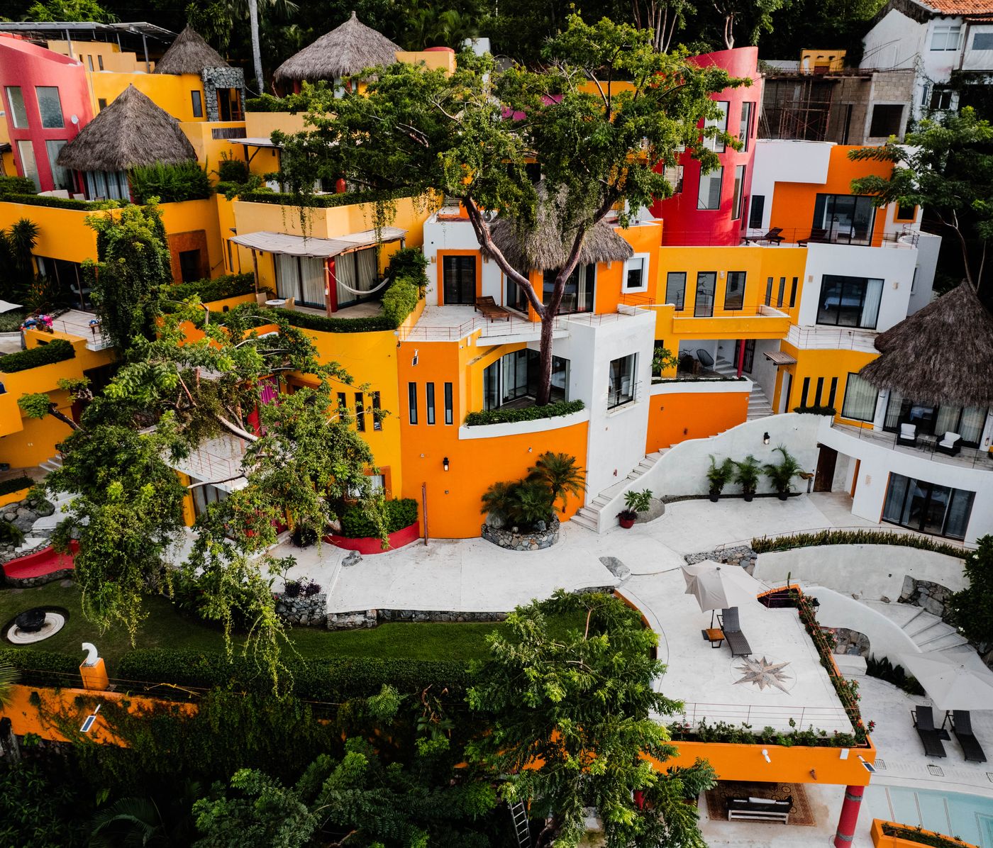 Aerial view of orange and white villas, pools and palapa roofs among tropical trees at Villa Mandarinas