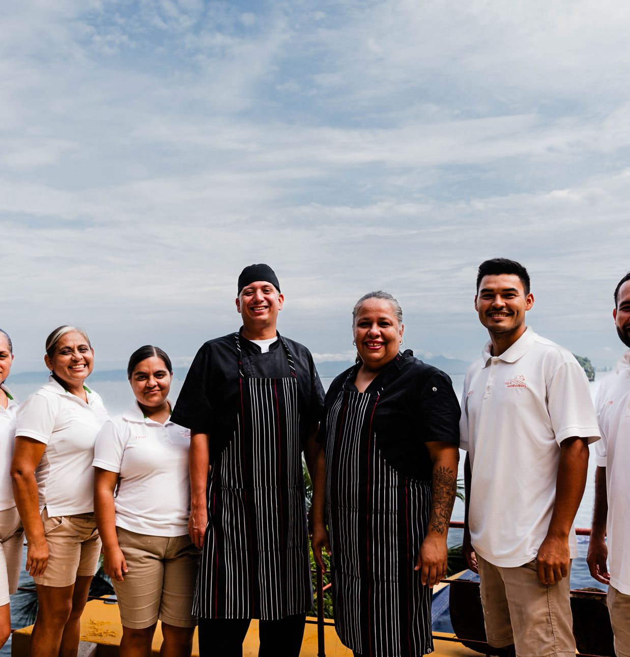 Villa Mandarinas staff team standing together on a terrace with the ocean behind them