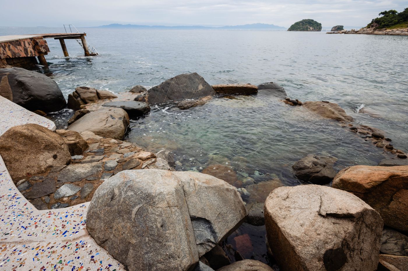 Rocky tide pools on the shore with the Los Arcos islets in the bay