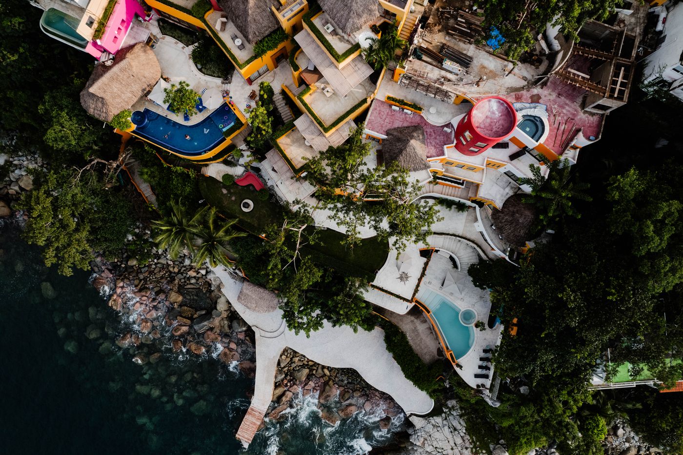 Top-down aerial view of the Villa Mandarinas estate on the cliff, with pools, terraces, pier and rocky shore