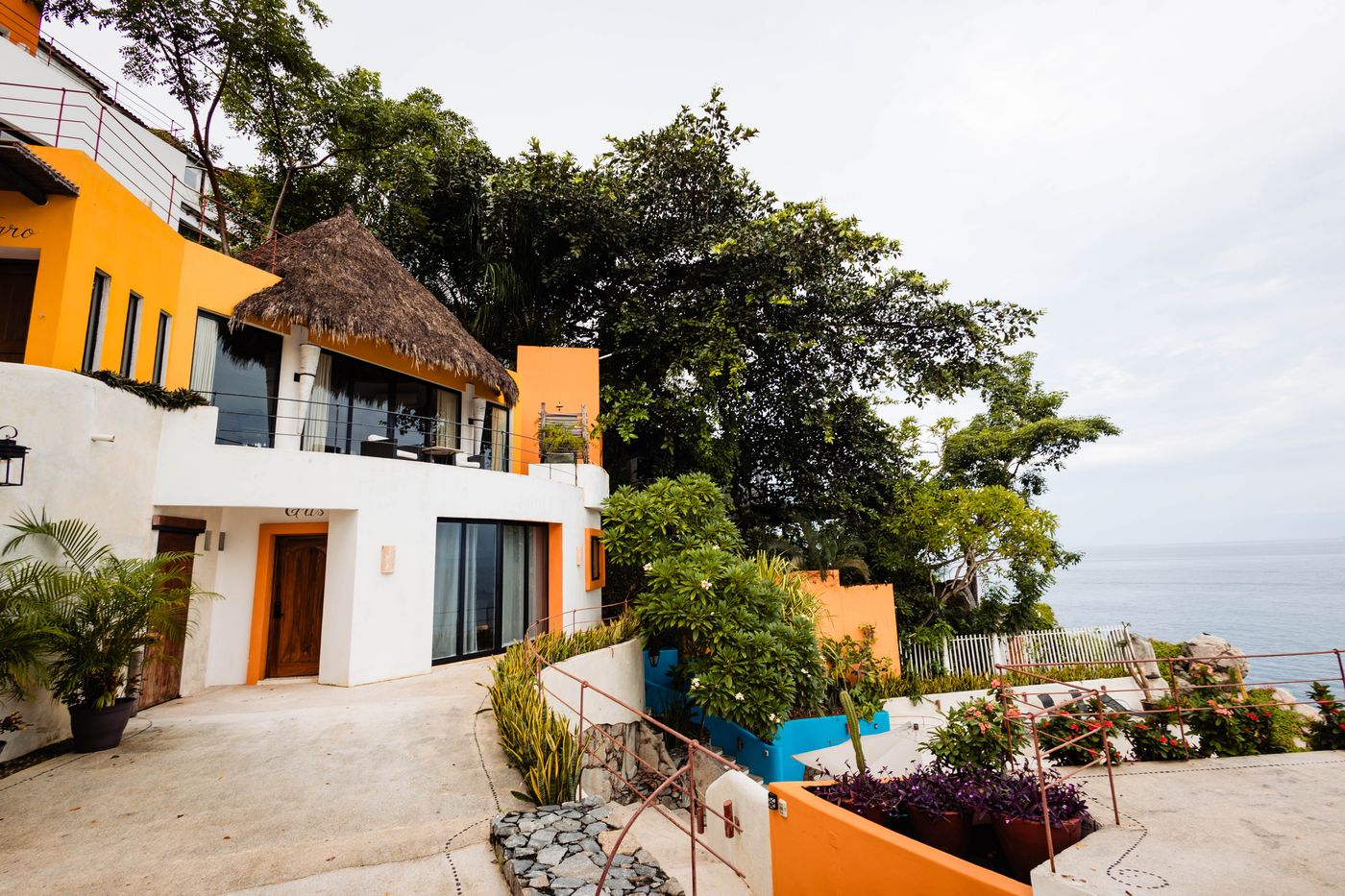 White and orange villa with a thatched palapa roof under a blue sky