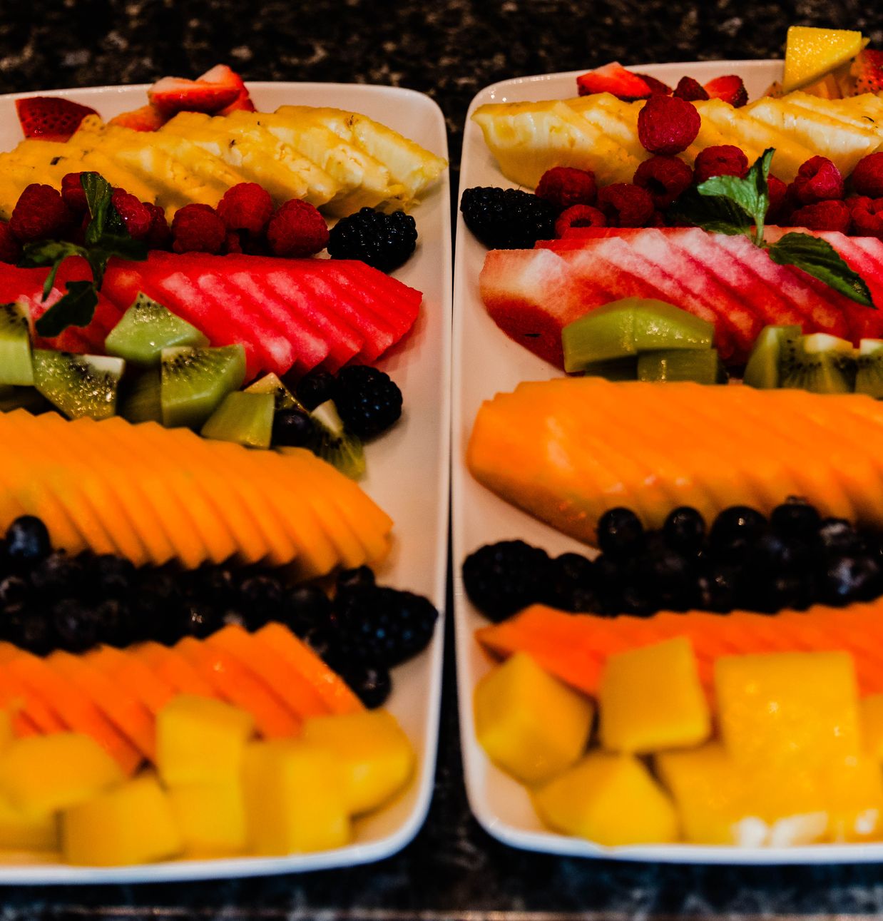 Two platters of fresh sliced fruit including watermelon, papaya, pineapple, kiwi and berries