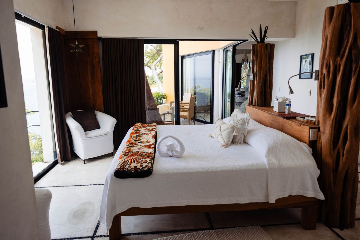 Bedroom with a white bed, carved wood posts and a window with an ocean view at Villa Mandarinas