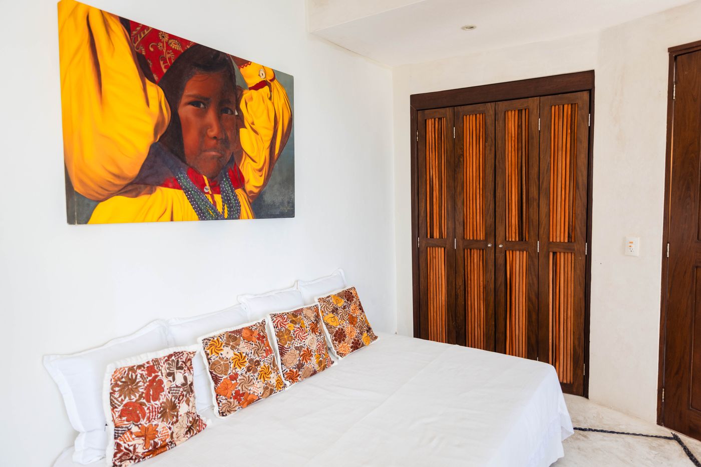Bedroom with patterned pillows and a large painting of a woman in yellow at Villa Mandarinas