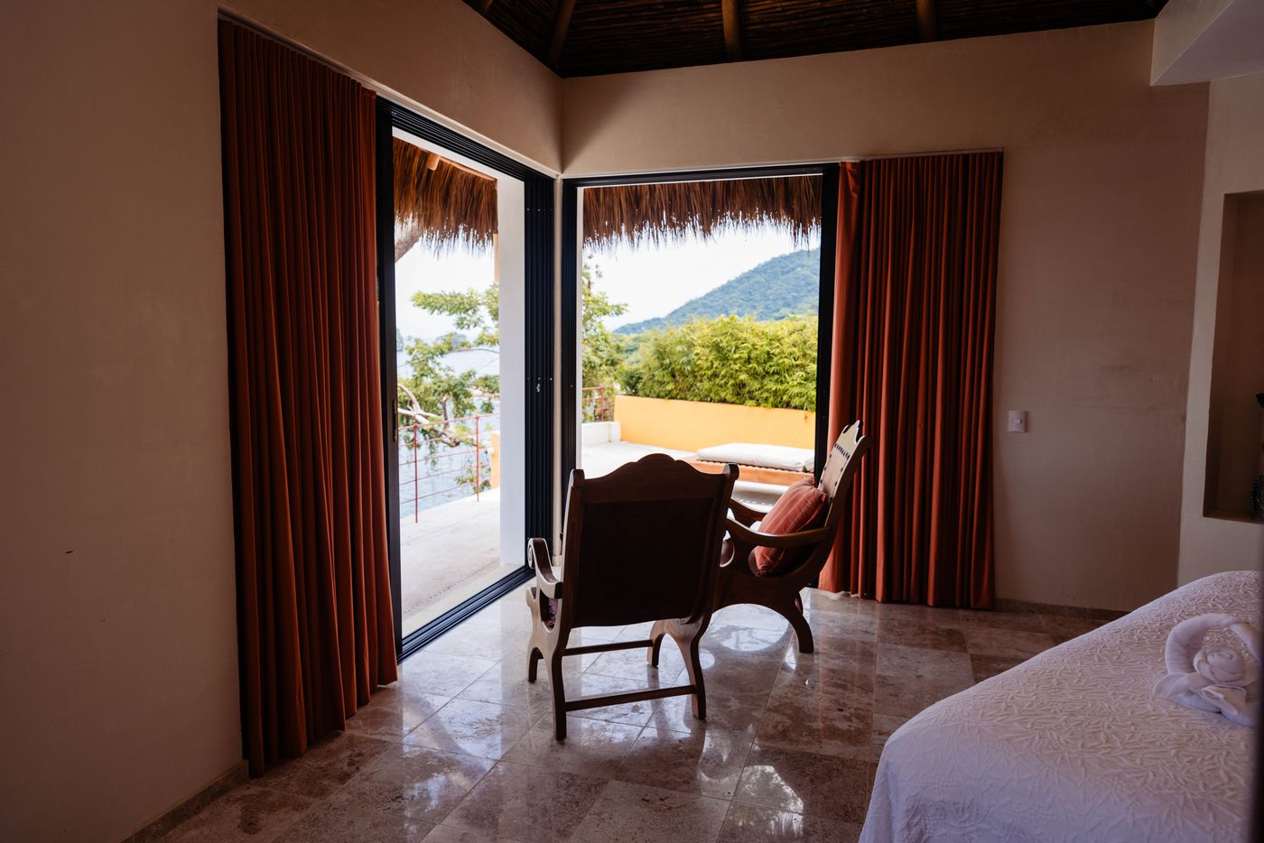 Bedroom with red curtains, a palapa ceiling and a chair by the terrace doors at Villa Mandarinas