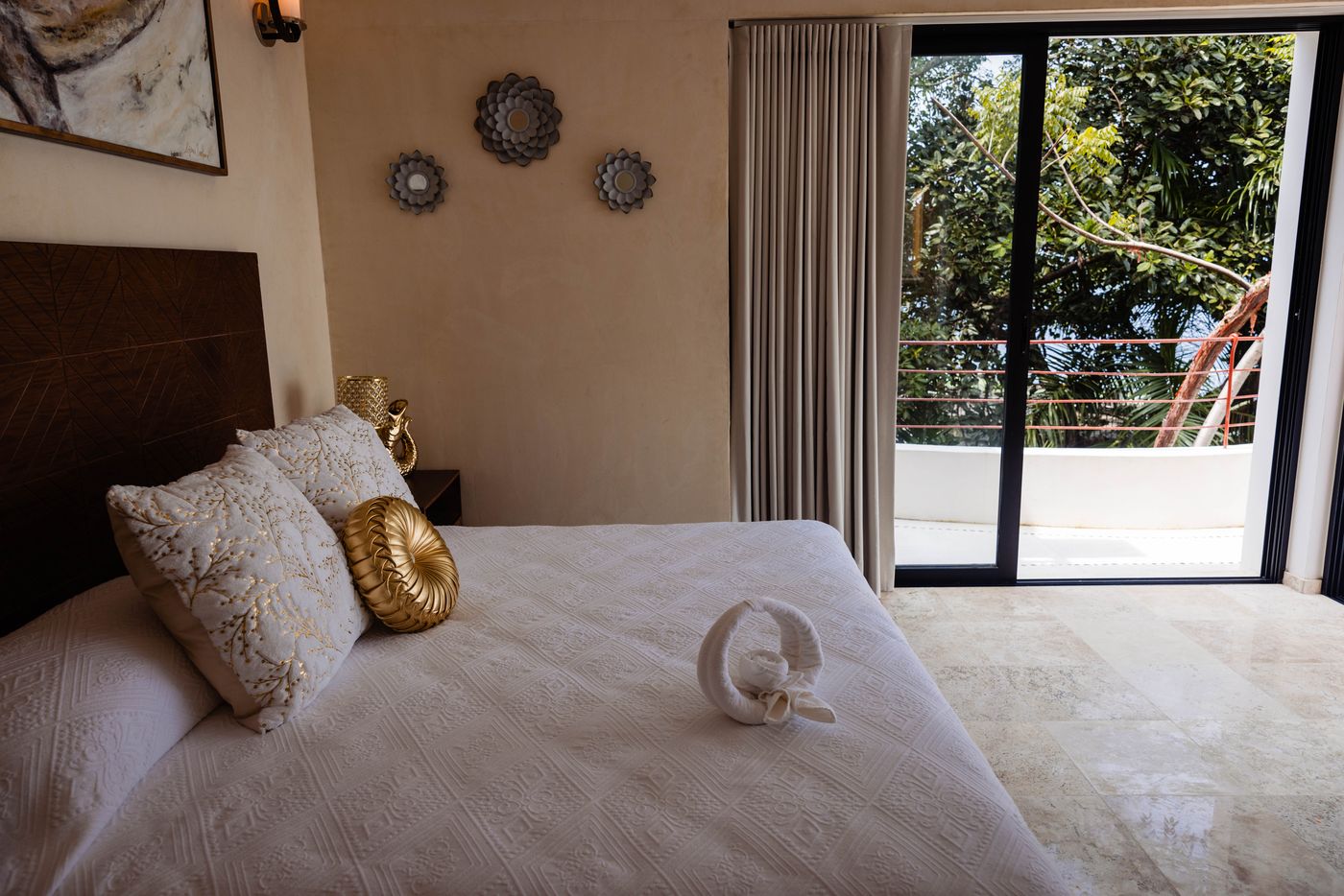 Bed with pillows beside sliding doors to a terrace and trees at Villa Mandarinas